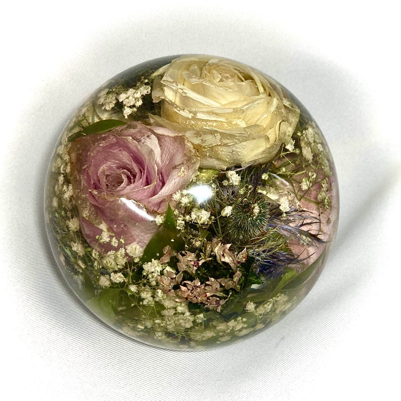 A stunning wedding bouquet preserved inside a large clear resin sphere. The delicate flowers, leaves, and stems are perfectly encased, creating a timeless and unique display piece. Perfect for reliving special memories and adding a touch of elegance to any room.