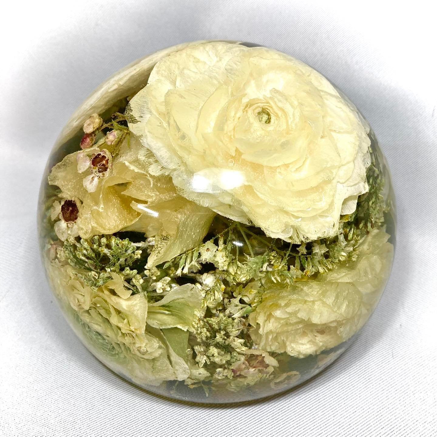 A stunning wedding bouquet preserved inside a large clear resin sphere. The delicate flowers, leaves, and stems are perfectly encased, creating a timeless and unique display piece. Perfect for reliving special memories and adding a touch of elegance to any room.