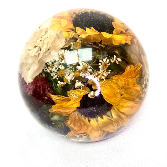 A stunning wedding bouquet preserved inside a large clear resin sphere. The delicate flowers, leaves, and stems are perfectly encased, creating a timeless and unique display piece. Perfect for reliving special memories and adding a touch of elegance to any room.