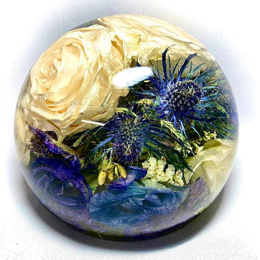 A stunning wedding bouquet preserved inside a large clear resin sphere. The delicate flowers, leaves, and stems are perfectly encased, creating a timeless and unique display piece. Perfect for reliving special memories and adding a touch of elegance to any room.