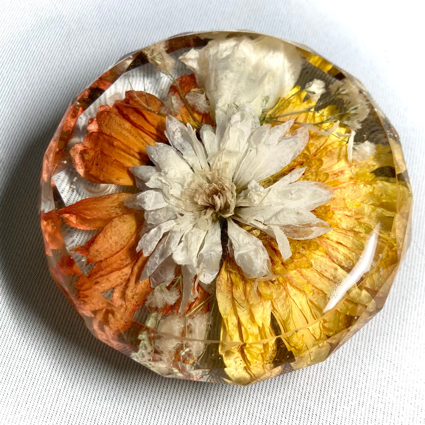 Faceted drinks coaster featuring a yellow half gerbera, a orange half gerbera with a white chrysanthemum in the center offset with gypsophila and a white lisianthus