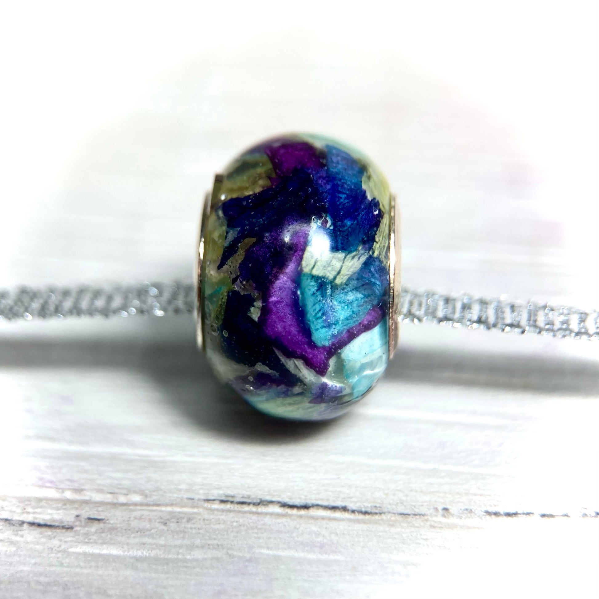 A stunning charm bracelet bead featuring preserved wedding flower petals encased in clear resin with a gleaming sterling silver core. The petals, captured forever in time, serve as a cherished memento of a special day and symbolize the beauty and love of the occasion. A perfect keepsake to wear every day and remember the joy of the wedding day.