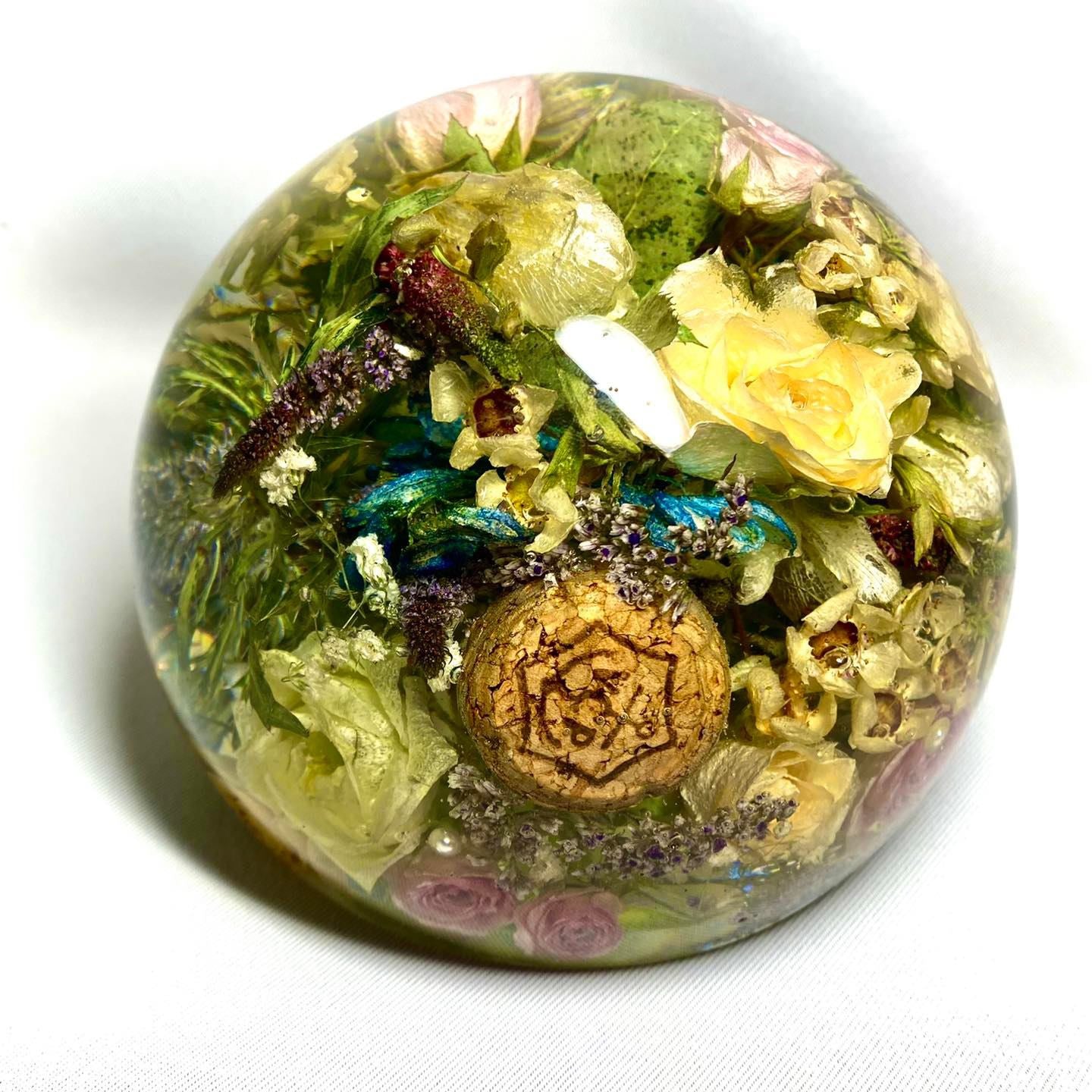 A stunning wedding bouquet preserved inside a large clear resin sphere. The delicate flowers, leaves, and stems are perfectly encased, creating a timeless and unique display piece. Perfect for reliving special memories and adding a touch of elegance to any room.