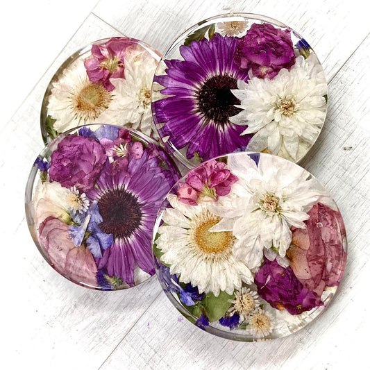 A clear, resin coaster featuring preserved wedding flowers encased within its surface. The round coaster showcases a bouquet of delicate blooms in vibrant colors, adding a touch of elegance to any tabletop.