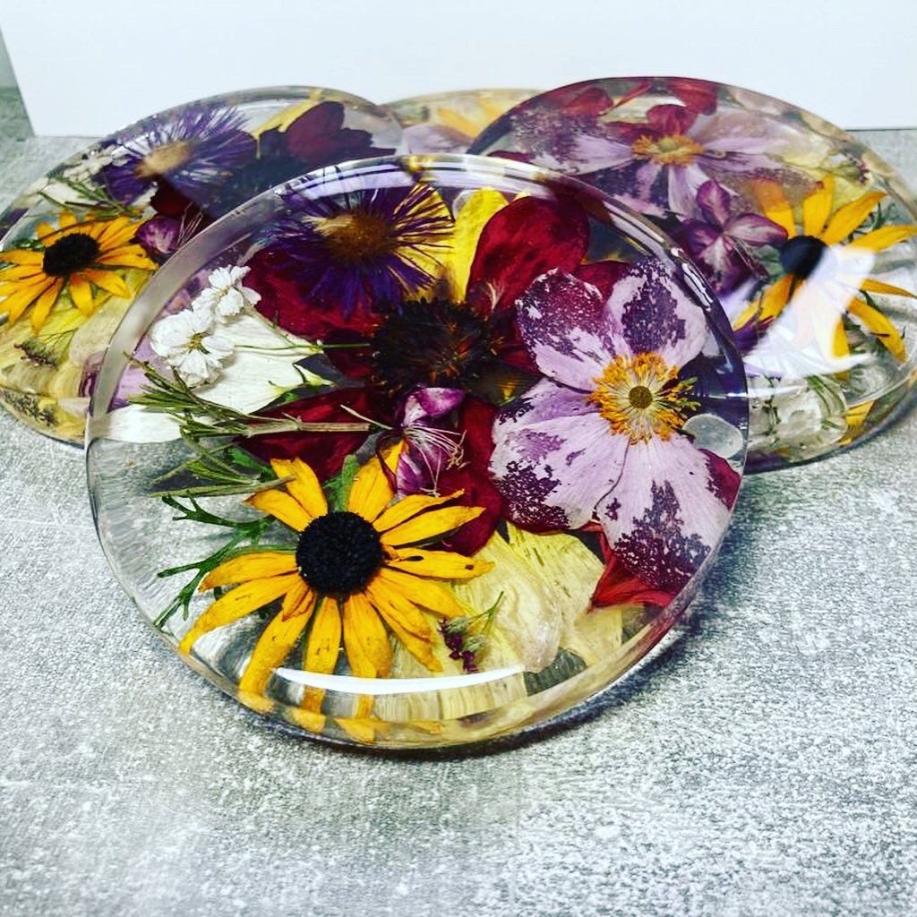 A clear, resin coaster featuring preserved wedding flowers encased within its surface. The round coaster showcases a bouquet of delicate blooms in vibrant colors, adding a touch of elegance to any tabletop.,