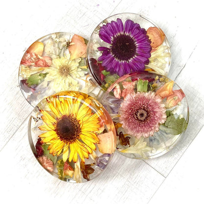 A clear, resin coaster featuring preserved wedding flowers encased within its surface. The round coaster showcases a bouquet of delicate blooms in vibrant colors, adding a touch of elegance to any tabletop.