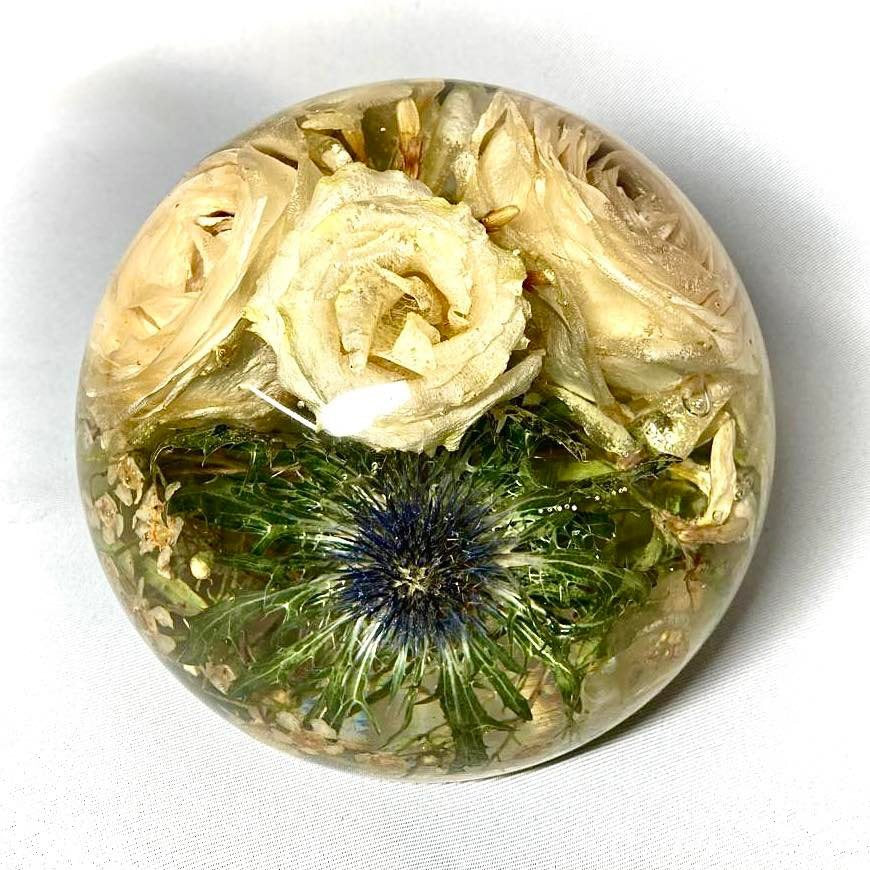 A stunning wedding bouquet preserved inside a large clear resin sphere. The delicate flowers, leaves, and stems are perfectly encased, creating a timeless and unique display piece. Perfect for reliving special memories and adding a touch of elegance to any room.