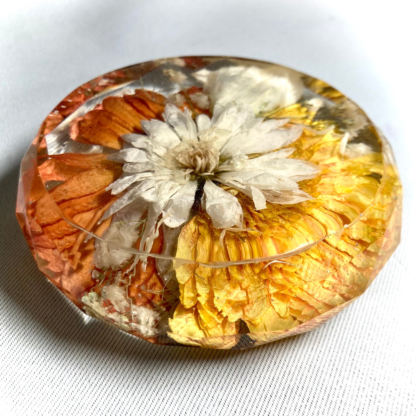 Faceted drinks coaster featuring a yellow half gerbera, a orange half gerbera with a white chrysanthemum in the center offset with gypsophila and a white lisianthus
