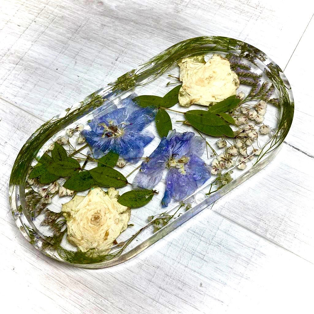 Oval jewellery tray containing delphinium and pressed white roses and foliage