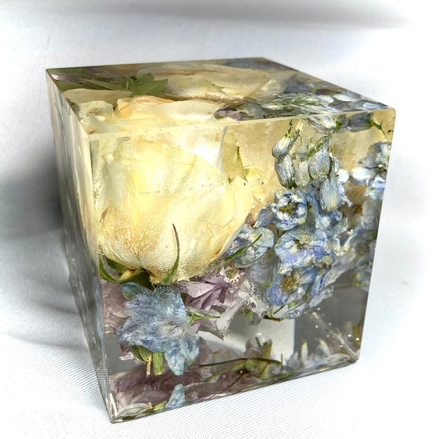 8cm cube containing two small peach roses, pale blue delphinium pink blossom