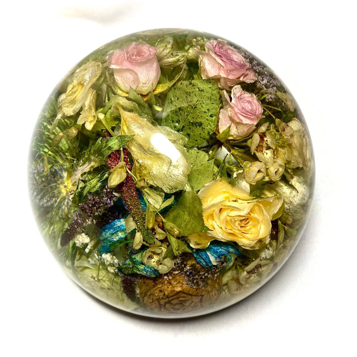 A stunning wedding bouquet preserved inside a large clear resin sphere. The delicate flowers, leaves, and stems are perfectly encased, creating a timeless and unique display piece. Perfect for reliving special memories and adding a touch of elegance to any room.