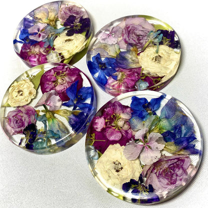 A clear, resin coaster featuring preserved wedding flowers encased within its surface. The round coaster showcases a bouquet of delicate blooms in vibrant colors, adding a touch of elegance to any tabletop.