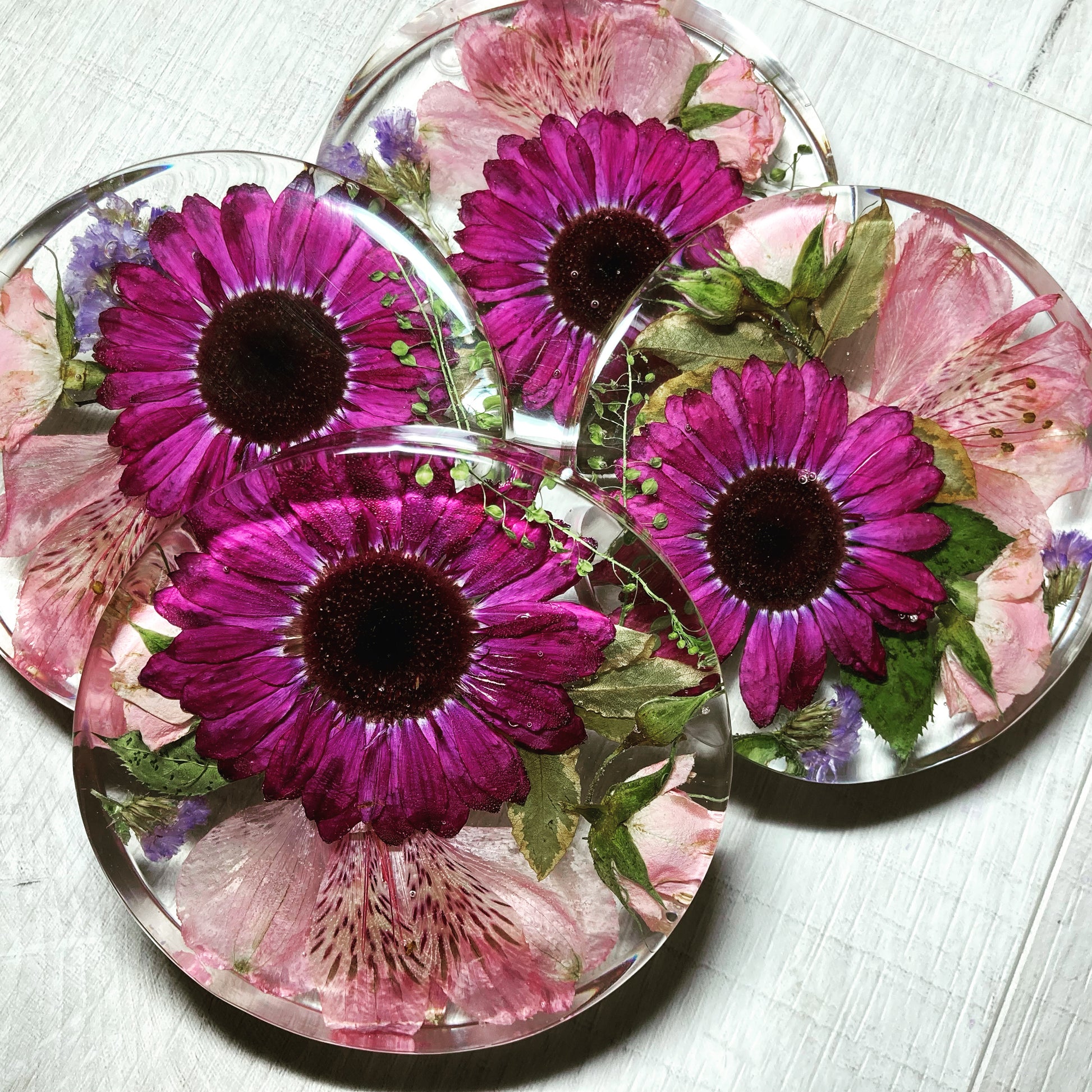 A clear, resin coaster featuring preserved wedding flowers encased within its surface. The round coaster showcases a bouquet of delicate blooms in vibrant colors, adding a touch of elegance to any tabletop.